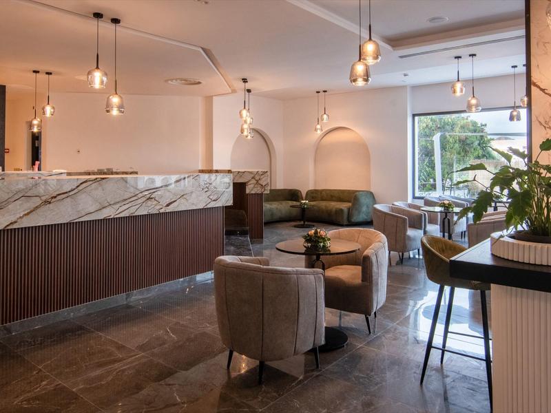 Área de salón moderno de hotel con mostrador de mármol, zonas de asientos y grandes ventanas para luz natural.