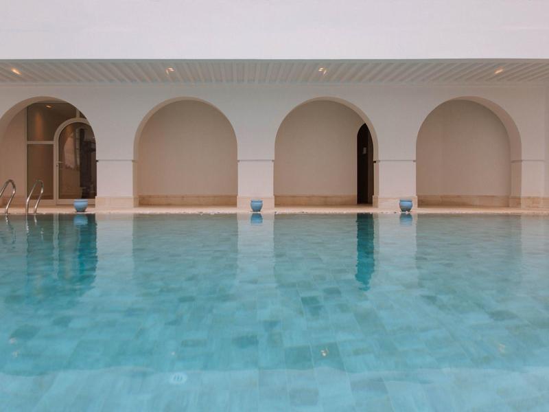 Gran piscina frente a una pared blanca con cuatro arcos en un hotel o resort.