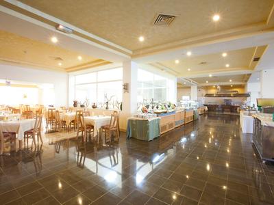 Weitläufiger Speisesaal mit Tischen, Stühlen und einem Buffetbereich in warmem Licht.