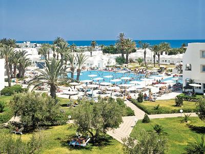 Hotelanlage mit Pool, Liegestühlen und Palmen, Meer im Hintergrund unter klarem Himmel.