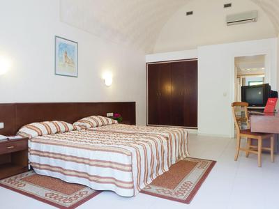 Helles Hotelzimmer mit Doppelbett, Schreibtisch, Stuhl, Fernseher und kleinem Schrank.