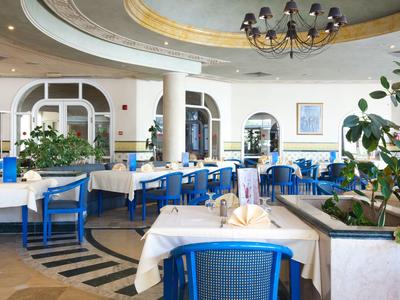 Helles Restaurant mit blauen Stühlen, weißen Tischen und grünen Pflanzen in einem Hotel.