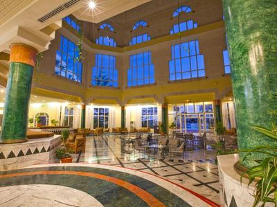 Helle Hotellobby mit grün marmorierten Säulen und großen Fenstern bei Dämmerung.