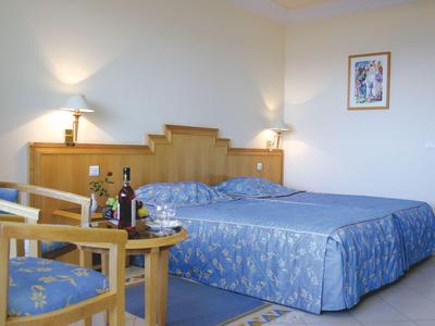 Helles Hotelzimmer mit Doppelbett, blauen Bettdecken und Holzmöbeln mit Tisch und Stühlen.