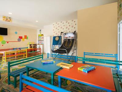 Bunter Kinderspielraum mit Tischen, Stühlen und Fernseher in einem hellen Raum.