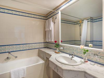 Helles Badezimmer mit Badewanne, Waschbecken, großem Spiegel und floral dekoriertem Waschbeckenbereich.