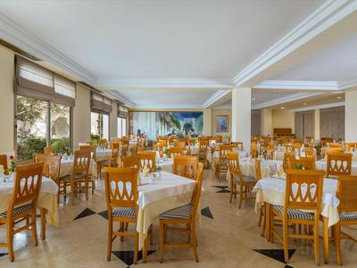 Großer Speisesaal mit vielen Holztischen und Stühlen, gedeckt mit weißen Tischdecken.