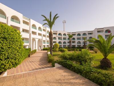 Innenhof eines Hotels mit Palmen, gepflegtem Grün und weißem Gebäude mit bogenförmigen Fenstern.