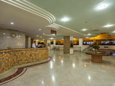 Großer, heller Hotellobbybereich mit Rezeption, Marmorboden und dezenter Beleuchtung.