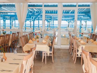 Helles Restaurant mit Holztischen und Stühlen, Blick auf Meer durch große Fenster