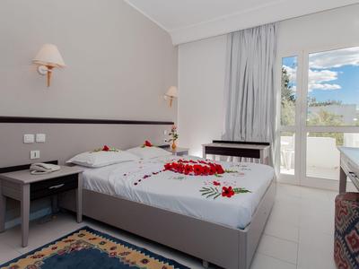 Hell eingerichtetes Hotelzimmer mit Doppelbett und Balkon, dekoriert mit roten Rosenblättern.