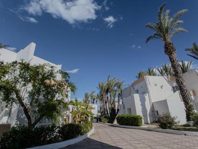 Moderner Hotelkomplex mit weißem Anstrich, Palmen und blauem Himmel an einem sonnigen Tag.