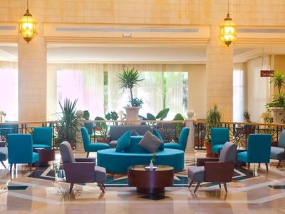 Elegante Hotellobby mit blauen Sesseln, Rundtischen und großen Fenstern mit Blick auf Pflanzen.