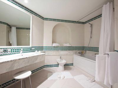 Helles Badezimmer mit großer Badewanne, Waschbecken, Toilette und dekorativem grün-weißem Fliesenmuster.