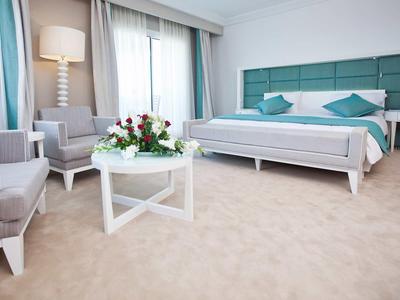 Helles Hotelzimmer mit Doppelbett, zwei Sesseln und einem Tisch mit Blumenarrangement