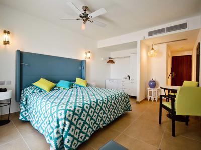 Helles Schlafzimmer mit großem Bett, blau-grünem Muster, zwei bunten Kissen und moderner Beleuchtung.