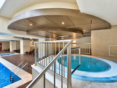 Innenbereich mit runder Whirlpool-Badewanne, Schwimmbecken, Treppe und Deckendesign in Beige und Blau.
