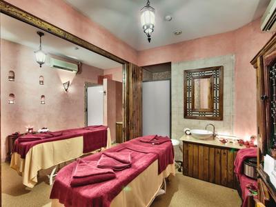 Gemütlicher Raum mit rosafarbenen Wänden und zwei Massagebetten mit roten Decken.