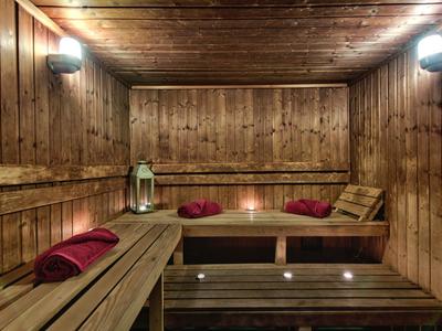Holzsauna mit Holzbänken, roten Handtüchern, Laterne und gedämpftem Licht an der Decke.
