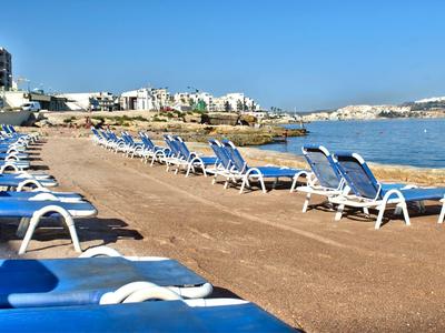 Viele weiße und blaue Liegestühle stehen auf einer breiten Promenade am Meer bei klarem Himmel.