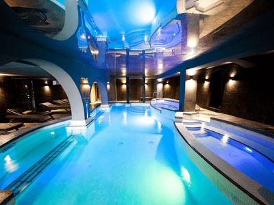 Moderner Indoor-Pool mit blauem Wasser, Beleuchtung und Liegeflächen auf beiden Seiten.