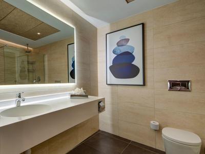 Helles Badezimmer mit beleuchtetem Spiegel, moderner Toilette und Kunstbild an beiger Wand.