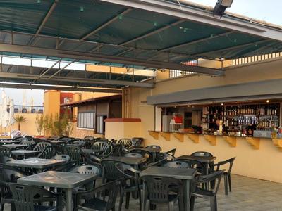 Leerer Außenbereich eines Cafés mit schwarzen Kunststofftischen und -stühlen unter grünem Dach.