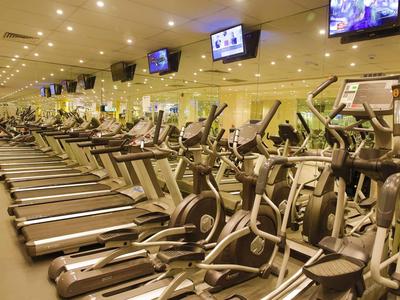 Großer Fitnessraum mit zahlreichen Laufbändern und Crosstrainern, viele Bildschirme an der Decke.
