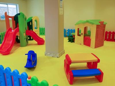 Bunter Innen-Kinderspielplatz mit Rutsche, Häuschen und Sitzbank, umgeben von Kunststoffzaun.