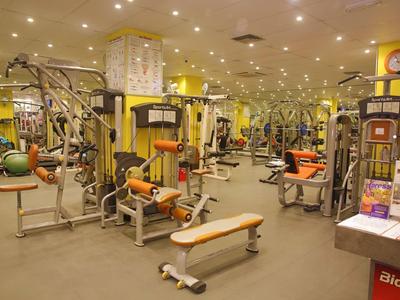 Großer Fitnessraum mit vielfältigen weißen und orangefarbenen Trainingsgeräten und hellem Licht.