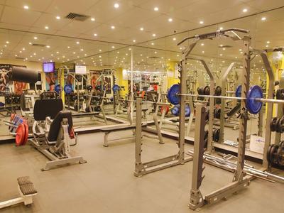 Großer Fitnessraum mit vielen Trainingsgeräten, Spiegelwänden und beleuchtetem Deckengehäuse.