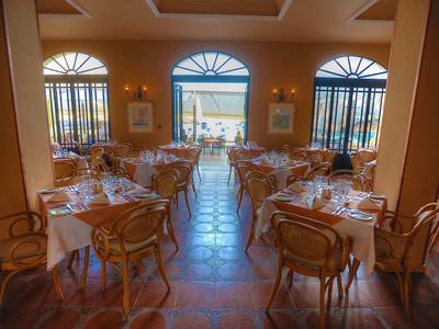 Elegantes Restaurant mit Holzmöbeln, weißen Tischdecken und Blick auf das Meer durch große Fenster.