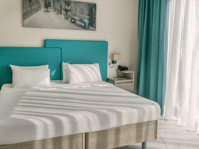 Helles Schlafzimmer mit großem Bett, türkisfarbenem Kopfteil, weißen Kissen und Vorhängen.
