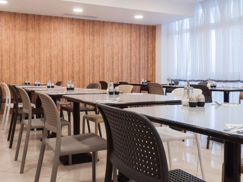 Moderner Konferenzraum mit rechteckigen Tischen, schwarzen Stühlen und hellen Holzpaneelen an der Wand.