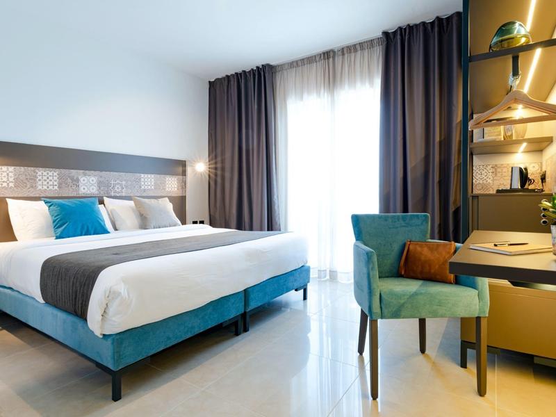 Modern eingerichtetes Schlafzimmer mit großem Bett, samtblauem Sessel und praktischem Schreibtisch.