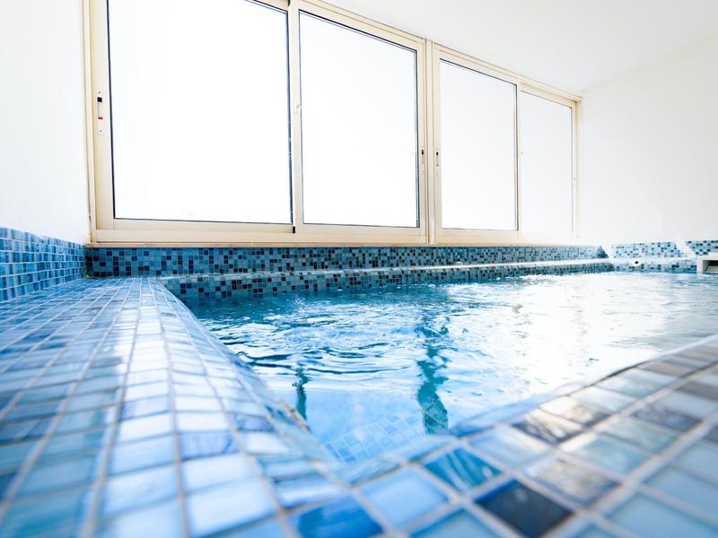 Ein kleines Schwimmbecken mit blauen Mosaikfliesen und großen Fenstern im Hintergrund.