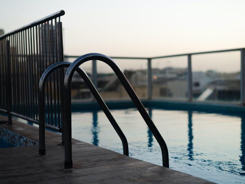 Schwimmbad mit Metallleiter, ruhigem Wasser und Geländer bei Abendlicht.