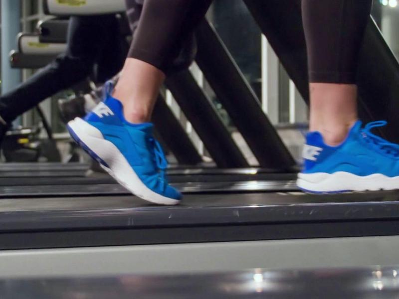 Blaue Sportschuhe an Füßen laufen auf Laufband in modernem Fitnessstudio mit Spiegelwand.