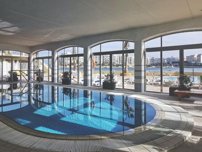 Hallenbad mit großen Glasfenstern und Blick auf eine Stadt bei klarem Wetter.