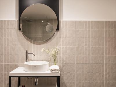 Bagno moderno con specchio rotondo, lavabo sopra il tavolo e piastrelle murali in tonalità neutre.