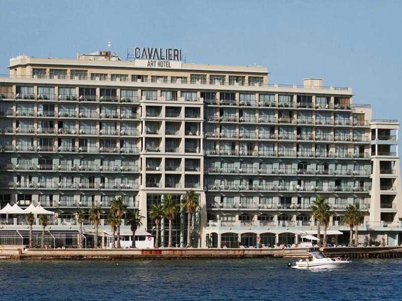 Grande edificio dell'hotel con molti balconi direttamente sull'acqua e una barca davanti.