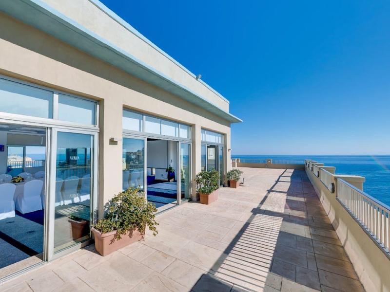 Balcone con finestre in vetro e vista sul mare sotto un cielo limpido.