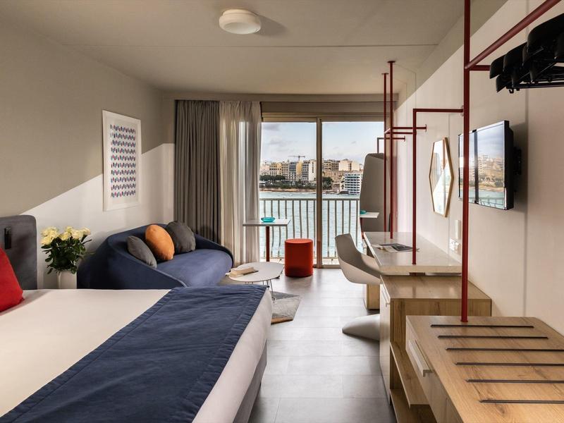 Camera d'hotel moderna con letto matrimoniale, divano, finestra con vista sulla città e scrivania.