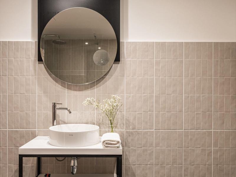 Bagno moderno con specchio rotondo, lavabo sopra il tavolo e piastrelle murali in tonalità neutre.