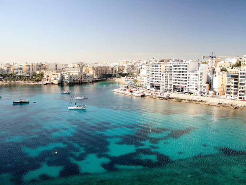 Acqua di mare limpida davanti a una città costiera moderna con edifici bianchi e barche.