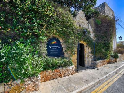 Hoteleingang in Steinmauer mit grünem Bewuchs und blauem Schild am Straßenrand.
