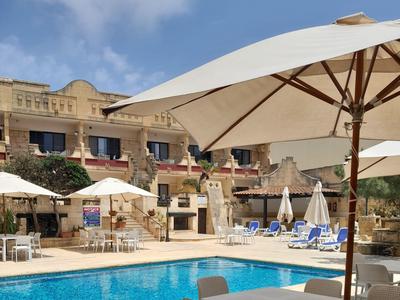 Hotelpoolbereich mit Sonnenschirmen, Liegestühlen und einem historischen Gebäude im Hintergrund.