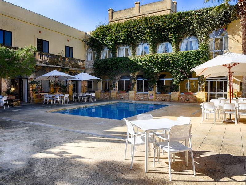 Binnenplaats van een hotel met zwembad, parasols en tafels in de schaduw.