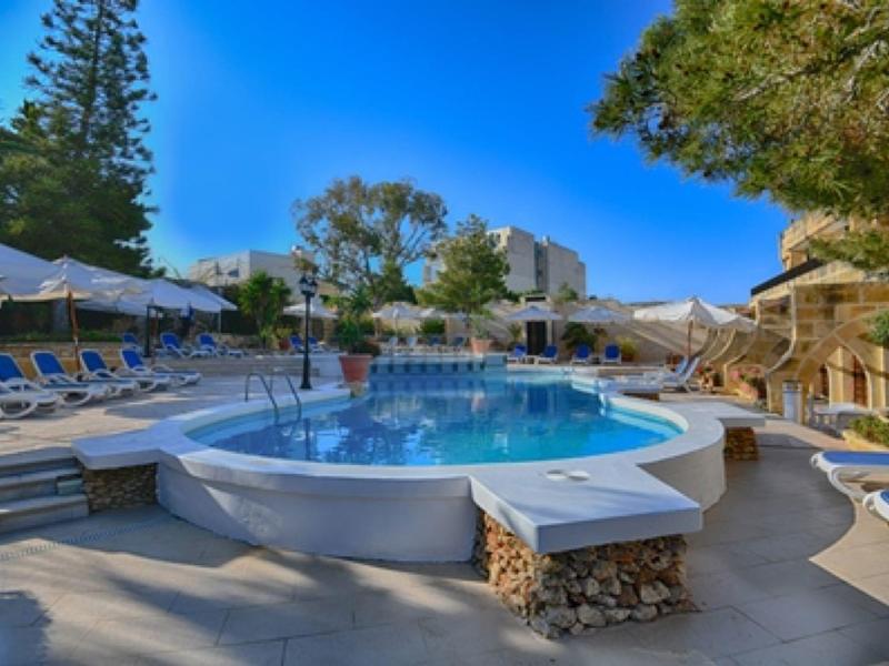 Ronde buitenzwembad met ligstoelen en bomen onder een heldere blauwe lucht.