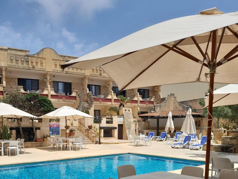 Hotelzwembad met ligstoelen en parasols voor een traditioneel gebouw onder een zonnige hemel.